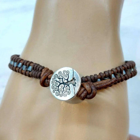 The Tree of Life Button Brown Gray Leather Wrap Seed Bead Bracelet by Alexa Martha Designs features a braided leather band and a silver tree of life button clasp, shown worn on a wrist.