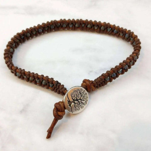 The Alexa Martha Designs Tree of Life Button Brown Gray Leather Wrap Seed Bead Bracelet features a round silver tree charm, beautifully displayed on a white marble surface.