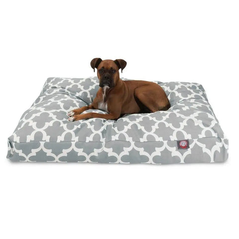 A brown dog with a black snout lies on the Majestic Pet Trellis Rectangle Dog Bed. The bed features a gray and white geometric pattern, washable cover, premium polyester fill, and has a small red tag on the front. The dog is looking forward.