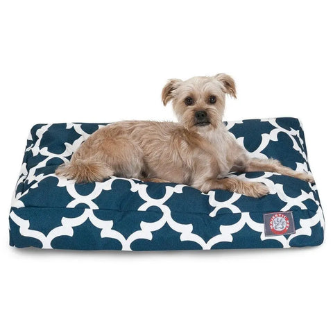A small tan dog with wiry fur lies on a Majestic Pet Trellis Rectangle Dog Bed, featuring a blue and white pattern and premium polyester fill, looking toward the camera.