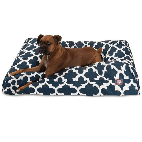 A brown dog is lying on the Majestic Pet Trellis Rectangle Dog Bed, which features a navy blue and white geometric design and premium polyester fill. The dog appears relaxed and is looking slightly to the side.