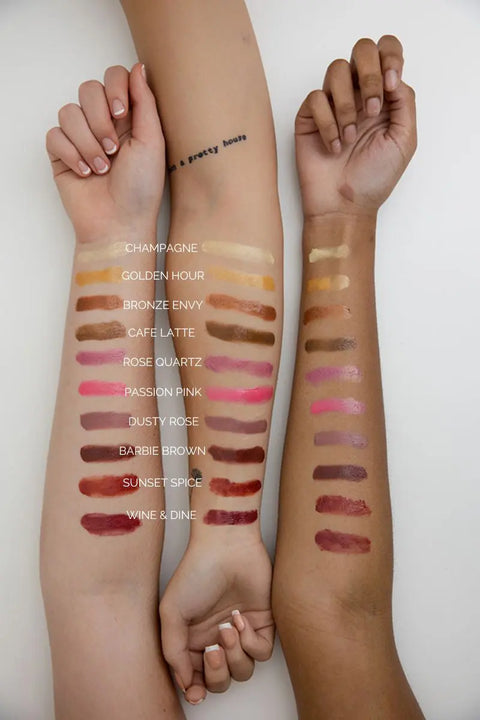 Three forearms with varying skin tones display swatches of Cheryl Kelly & Co.’s Triple Tint Therapy in ten shades: Champagne, Golden Hour, Bronze Envy, Caffè Latte, Rose Quartz, Passion Pink, Dusty Rose, Barbie Brown, Sunset Spice & Wine & Dine.