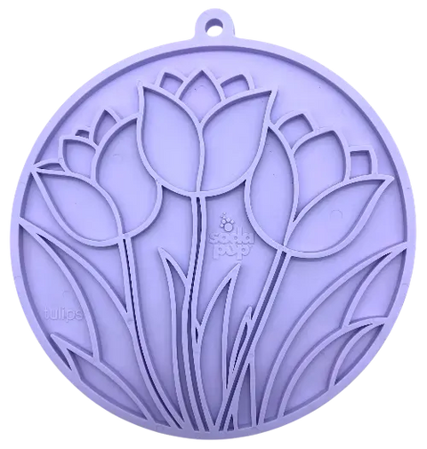 The Tulip Design EMat Enrichment Lick Mat With Suction Cups by SodaPup is a round, purple silicone mat featuring embossed tulip flowers and leaves, a hanging hole, and subtle branding. Perfect for calming your dog during snack time.