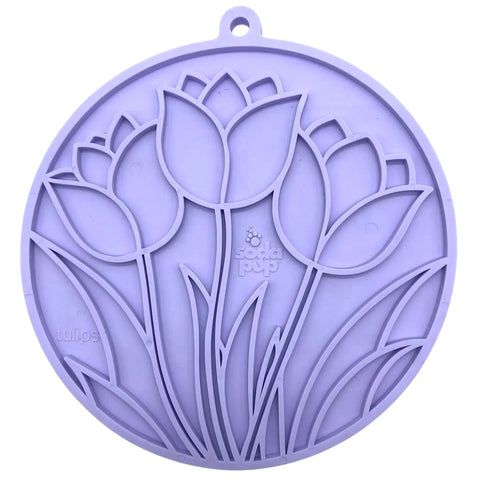 The Tulip Design EMat Enrichment Lick Mat by SodaPup is a round, lavender silicone mat with raised tulip outlines, embossed “tulips” and brand name, suction cups for grip, and a small hanging loop at the top.