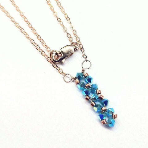 The Tiny Super Sparkly Rock Candy Crystal Bar Necklace by Alexa Martha Designs features a gold chain with a lobster clasp and a handmade pendant of blue beads and gold spacers—an elegant Swarovski crystal necklace for any occasion.