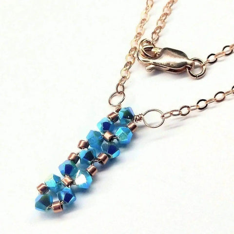 The Tiny Super Sparkly Rock Candy Crystal Bar Necklace by Alexa Martha Designs features a gold chain with faceted blue beads and metallic spacers, secured by a lobster clasp, and is displayed on a white background.