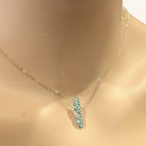 The Tiny Super Sparkly Rock Candy Crystal Bar Necklace by Alexa Martha Designs features a delicate gold chain and a bar pendant with sparkling crystals, beautifully displayed on a mannequin neck.