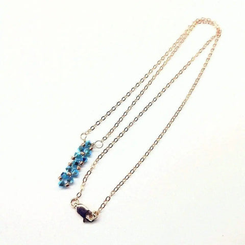 The Tiny Super Sparkly Rock Candy Crystal Bar Necklace by Alexa Martha Designs features a handmade gold chain with vertically clustered blue beads and a lobster clasp, showcased on a white background.