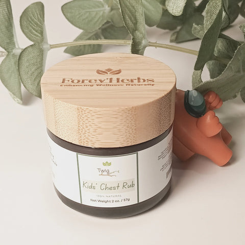 A jar of Twig - Kids' Chest Rub by Forev'Herbs with a bamboo lid sits on a white surface beside green leaves and an orange bear figurine holding a green stone.