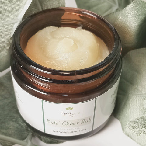 An open brown jar labeled Twig - Kids' Chest Rub by Forev'Herbs sits on soft green fabric, revealing creamy ointment inside. The 100% natural label notes its gentle formula and net weight of 2 oz (57g).