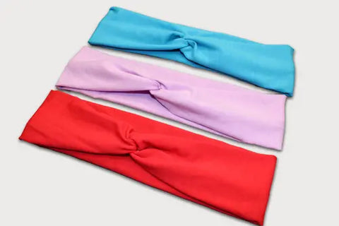 The Goodnighties Twist Headband 3-Pack features blue, light purple, and red fabric headbands with a center twist, made in the USA. These stylish accessories add flair to any outfit.