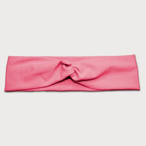 The Goodnighties Twist Headband in pink features a soft, lightweight fabric and a twisted knot center design, shown against a plain white background.