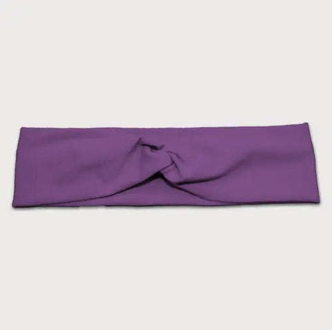 The Goodnighties Twist Headband, made in the USA, is a soft, lightweight purple hair accessory with a center knot. Shown on a white background, it combines comfort and style for any look.