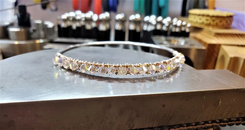 A delicate headband with clear, faceted beads is wire-wrapped along its length on a metal work surface with jewelry tools, reflecting the artistry of the Two Metal Embossed Wire Wrapped Crystal Bangle by Alexa Martha Designs.