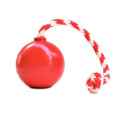 The SodaPup USA-K9 Cherry Bomb Durable Rubber Chew Toy is a red ball with a red and white braided rope, designed for tugging, training, playtime, retrieving, or dispensing treats—ideal as a versatile reward toy against a white background.
