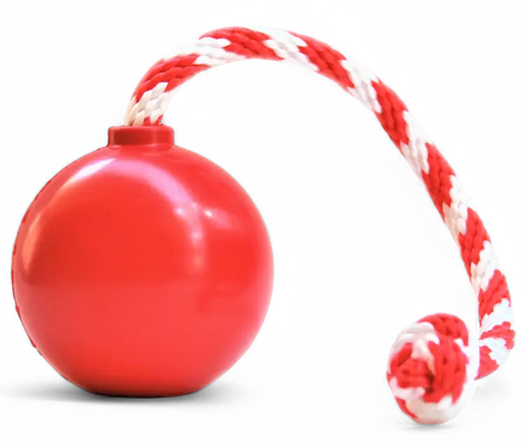 The SodaPup USA-K9 Cherry Bomb is a red durable rubber chew toy, treat dispenser, tug and retrieving toy with a red and white braided rope ending in a knot. Features a transparent background.