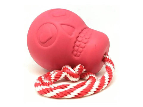 The SodaPup USA-K9 Skull is a pink, durable rubber chew toy featuring a sugar skull design. It functions as a treat dispenser, reward toy, tug toy, and retrieving toy, attached to a twisted red and white rope.