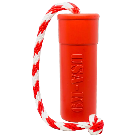 The SodaPup USA-K9 Firecracker Large Floating Rubber Dog Training Dummy is a red cylindrical tug toy with “USA-K9” embossed on the side, attached to a red and white braided rope knotted at the end. Made in the USA.