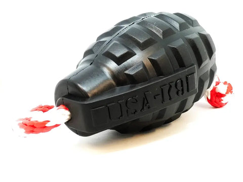 The SodaPup USA-K9 Magnum Grenade is a black, durable rubber chew toy for dogs. Shaped like a grenade with USA-19 embossed on the side and a red and white braided rope, its ideal as a treat dispenser, tug toy, or retrieving toy. Photographed on white background.