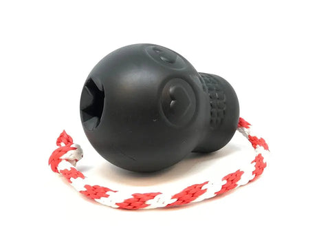 The SodaPup USA-K9 Magnum Skull Durable Rubber Chew Toy in black is a tough skull-shaped treat dispenser, reward toy, tug toy, and retrieving toy with carved features, attached to a red and white braided rope for hours of fun with your dog.