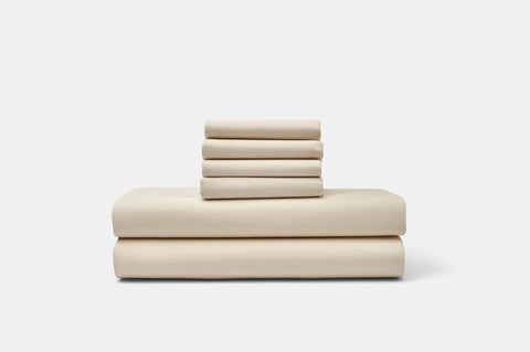 A neatly stacked set of American Blossom Linens Cotton Percale Bed Sheet Set, made from USA grown cotton, features two large sheets at the bottom and four folded pillowcases on top against a plain white background.
