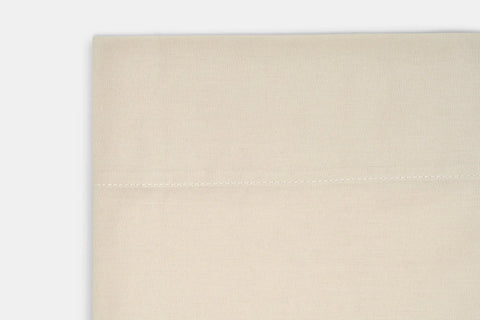 A close-up of luxurious beige cotton percale fabric from the American Blossom Linens Cotton Percale Bed Sheet Set, showing a horizontal seam and simple stitching against a white background.