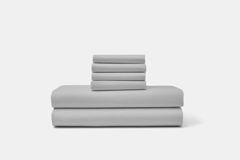 A neatly stacked American Blossom Linens Cotton Percale Bed Sheet Set in luxurious light gray, including sheets and pillowcases, arranged against a plain white background.
