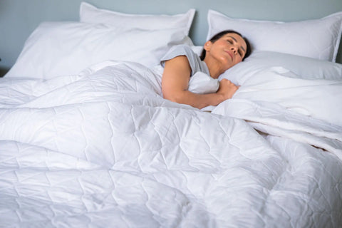 A woman sleeps peacefully on her side in bed with white pillows and an American Blossom Linens Cotton Quilted Bedspread, looking calm and comfortable.