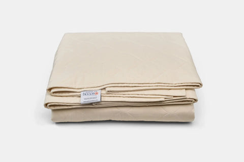 The Cotton Quilted Bedspread by American Blossom Linens in light beige features a diamond-stitched pattern and visible white fabric tag, offering eco-friendly luxury on a plain white surface.