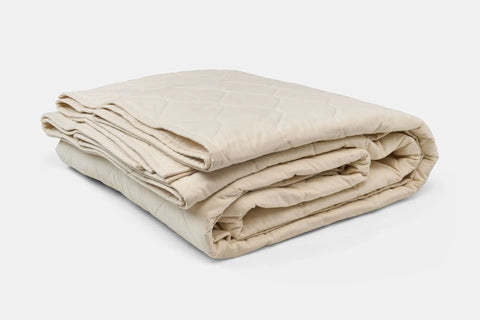 The American Blossom Linens Cotton Quilted Bedspread, in cream with a subtle diamond pattern, is made from USA-grown cotton for eco-friendly luxury and is neatly folded on a white background.