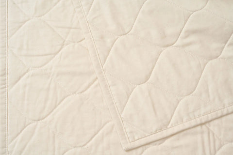 A close-up of a cream-colored, diamond-patterned Cotton Quilted Bedspread by American Blossom Linens, with one corner folded to show the same eco-friendly luxury design on both sides.