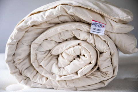 The Natural Wool Bedding Duvet Insert / Comforter by American Blossom Linens, shown rolled up on a light surface, is crafted from USA wool for heirloom quality—an ideal premium comforter or duvet insert for your bed.