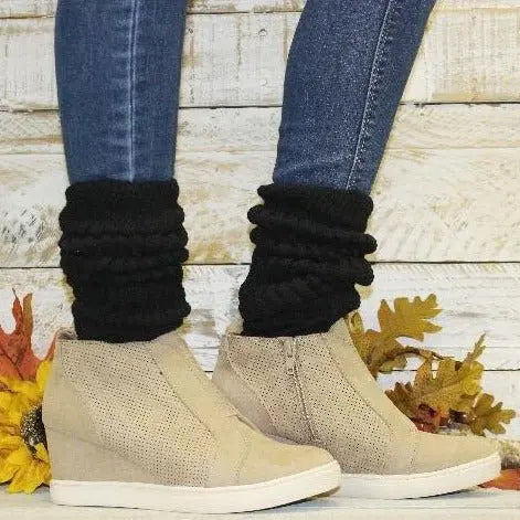 A person wears Catherine Cole ULTIMATE Cotton Slouch Socks for women in black, paired with blue skinny jeans and beige wedge ankle boots, standing before a wooden wall with autumn leaves scattered on the floor.