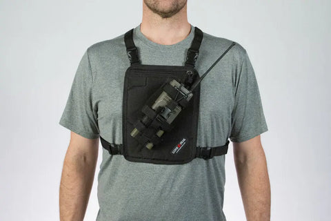 A person in a grey t-shirt models the Lone Peak Packs Universal Radio Chest Pack, featuring an adjustable radio pouch and hands-free harness with shoulder and chest straps, securely holding a radio on the front.