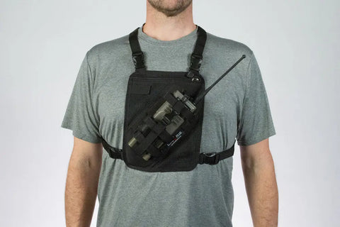 Wearing a gray t-shirt, a person sports the Lone Peak Packs Universal Radio Chest Pack—secured with adjustable straps and featuring handy pouches for a two-way radio and gear.
