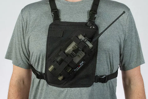 A person in a gray t-shirt wears the Lone Peak Packs Universal Radio Chest Pack, featuring an adjustable pouch that secures a handheld radio upright. The hands-free harness fits comfortably over the shoulders and around the chest.