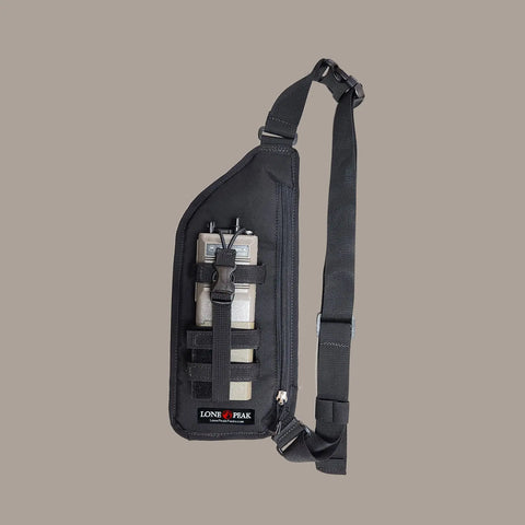 A black Lone Peak Packs Universal Sling Radio Holster with adjustable strap, front buckle, and three compartments is displayed against a plain gray background.