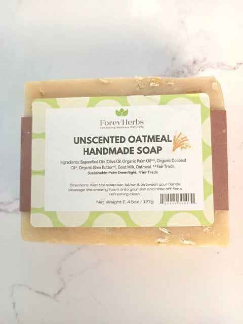 A beige bar of Unscented Oatmeal Handmade Soap by Forev'Herbs, labeled with natural ingredients like olive oil, coconut oil, goat milk, shea butter, and oatmeal, rests on a light surface.