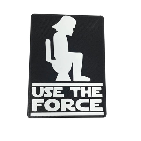 The Chatelet Manufacturing Use the Force Bathroom Sign - Funny Bathroom Signs - Black & White shows a white helmeted figure on a toilet with USE THE FORCE below—great as wall art or a gag gift.