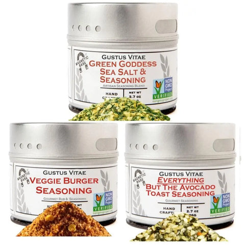 Three tins from vendor-unknown’s Veggie Lovers Seasonings - 3 Pack—Green Goddess Sea Salt & Seasoning, Veggie Burger Seasoning, and Everything But The Avocado Toast—are artfully displayed with their seasonings spilling in front.