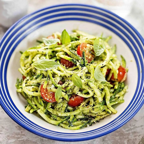 A bowl of zucchini noodles with pesto, cherry tomatoes, grated cheese, basil leaves, and a sprinkle of Veggie Lovers Seasonings - 3 Pack by vendor-unknown, served in a white bowl with blue stripes.