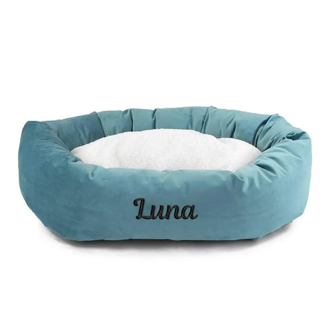The Majestic Pet Velvet Sherpa Bagel Dog Bed features a soft teal velvet exterior, a plush white cushion, and can be personalized with your dogs name on the front.
