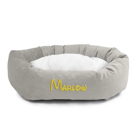 The Majestic Pet Velvet Sherpa Bagel Dog Bed - Personalized is a round gray velvet bed with a white cushioned center and Marlow embroidered in yellow, offering orthopedic comfort and support.