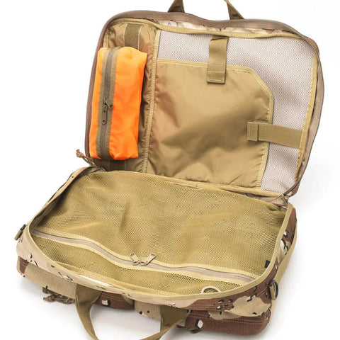 The MIS 3 Way Brief Bag in Chocochip Desert Camo is open, showing mesh compartments, a tan interior, and an attached orange zippered pouch. The water-resistant Cordura Nylon bag is empty and displayed against a white background.