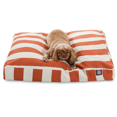 A small brown dog rests on the Majestic Pet Vertical Stripe Rectangle Dog Bed, featuring bold orange and white stripes and a washable cover for easy cleaning, while looking directly at the camera.