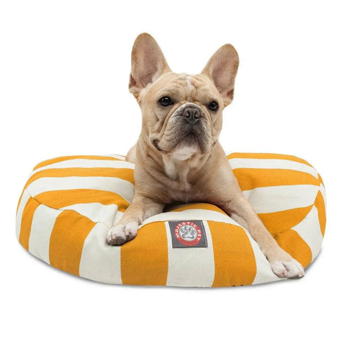 A light brown French Bulldog lies on the Majestic Pet Vertical Stripe Round Dog Bed with orange and white stripes, looking at the camera. The bed’s removable, washable cover allows for easy cleaning.