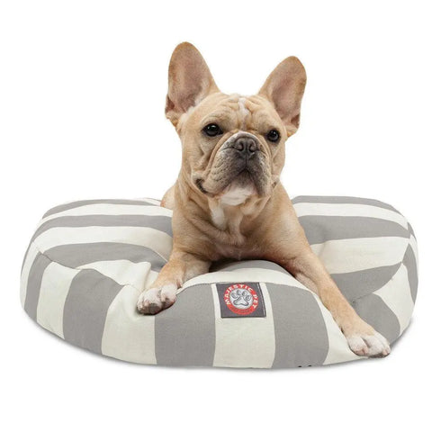 A light brown French Bulldog lies on the Majestic Pet Vertical Stripe Round Dog Bed, featuring gray and white stripes and a removable cover for easy cleaning. The dog looks forward with its ears perked up.