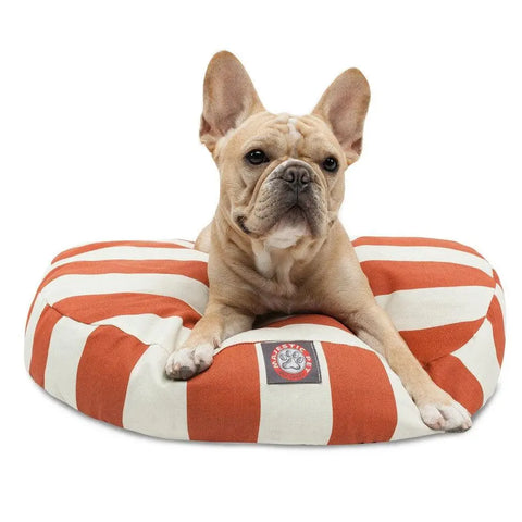 A light brown French Bulldog rests on the Majestic Pet Vertical Stripe Round Dog Bed, which has a red and white striped removable, washable cover and a front logo patch, gazing directly at the camera.