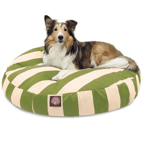 A Collie lies on a large Majestic Pet Vertical Stripe Round Dog Bed with wide green and beige stripes. The dog looks alert and relaxed, and a small patch with the dog logo appears on the bed’s removable cover.