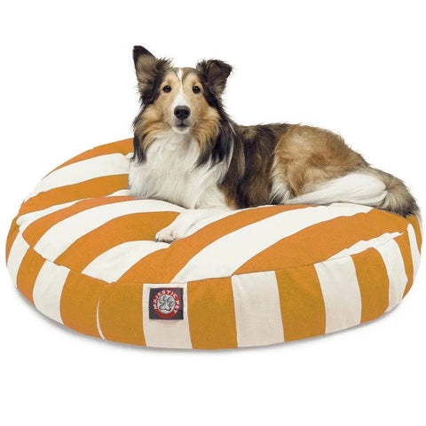 A Collie lies on the Majestic Pet Vertical Stripe Round Dog Bed, featuring orange and white stripes, a logo patch, and a washable removable cover. The relaxed dog looks directly at the camera.